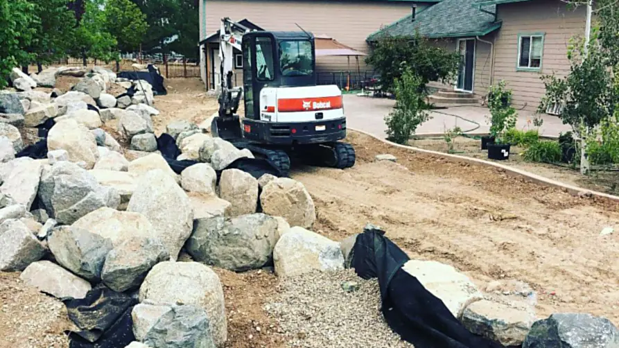 A granite boulder retaining wall under construction with drain rock behind it
