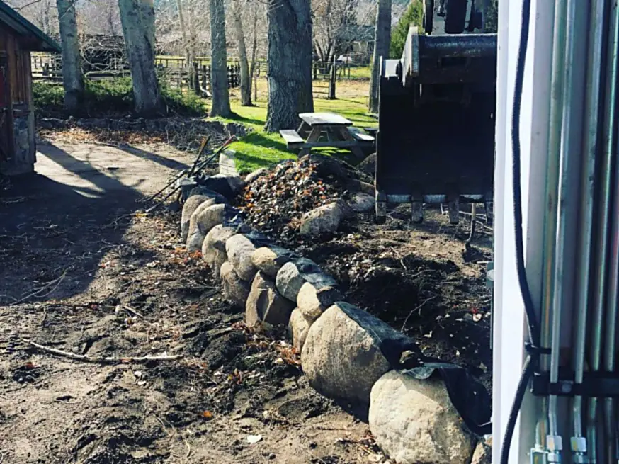 Drain rock and fabric going in behind a boulder wall before backfill